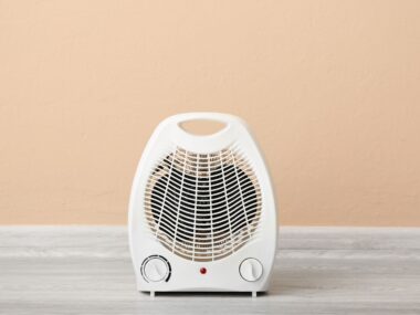 white fan heater on table with peach background